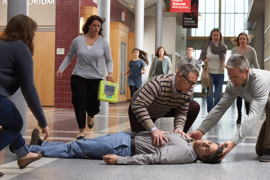 A group of people are looking at a person lying on the ground having Sudden cardiac arrest while a lady is running carrying a Zoll AED to provide first aid.