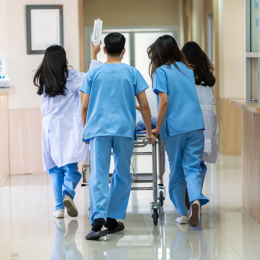Group of healthcare professionals in blue scrubs pushing a gurney in a hospital hallway.